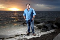 A photo shows Rodney Boblitt standing on a shoreline with sun low in the sky.