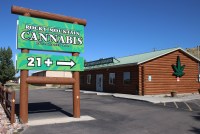 A outdoor large sign reads: "ROCKY MOUNTAIN CANNABIS 鈥� Established 2009 鈥� 21+" and points towards a cabin that has a large marijuana leaf on the side.