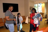 A photo of a mother holding a bundle of kids' clothes while two staff members help her.