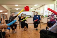 A photo of people sitting in chairs while using pool noodles to bounce a balloon in the air.