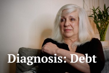 A still from a video of a woman seated. Text on the screen reads, "Diagnosis: Debt."