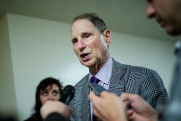 A photo of Senator Ron Wyden speaking into reporters' microphones at the Senate subway station inside the U.S. Capitol.