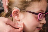 A photo of a person calibrating the hearing aid on a young girl.