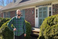 Patrick Dunnagan stands outside his North Carolina home on a sunny day. He wears a plaid shirt and glasses.