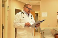A photo of a doctor standing indoors and looking at a binder.
